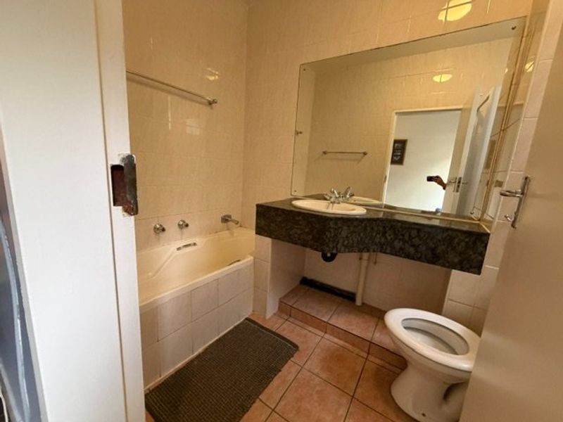 A dated bathroom featuring a bathtub, vanity with stone countertop, and tiled finishes. The space is functional but would benefit from modern updates.