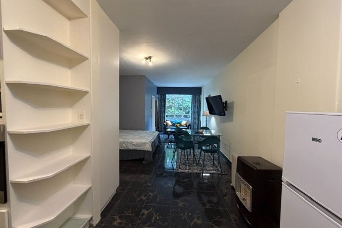 Open plan living area featuring dark tiled flooring, built-in shelving units, and a wall-mounted gas heater.