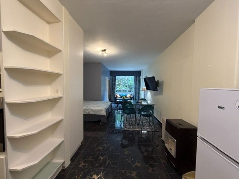 Open plan living area featuring dark tiled flooring, built-in shelving units, and a wall-mounted gas heater.