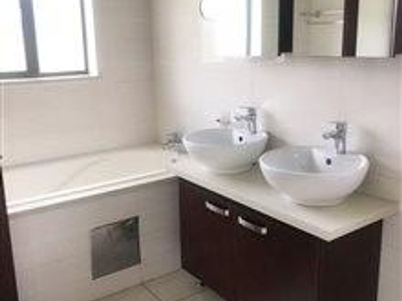 A clean, modern bathroom featuring a double vanity with vessel sinks, a built-in bathtub, and neutral wall tiling.
