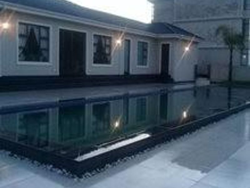 A modern townhouse exterior featuring a sleek swimming pool with dark tiling and a spacious paved patio area, perfect for outdoor relaxation.