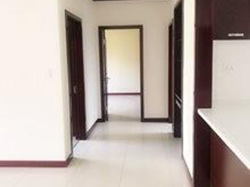 A bright, empty hallway featuring neutral tiled flooring and dark wood door frames, providing access to multiple rooms within the townhouse.