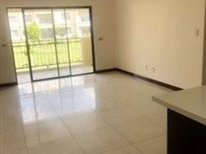 An empty open-plan living area featuring tiled flooring and a large sliding glass door providing access to an outdoor space.
