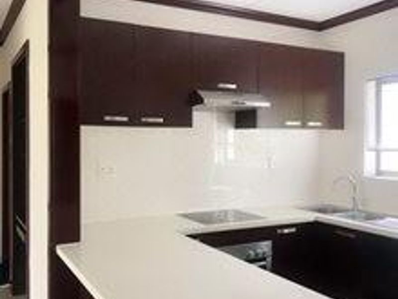 A modern kitchen featuring dark wood cabinetry, white stone countertops, a built-in oven, and a stainless steel extractor fan.