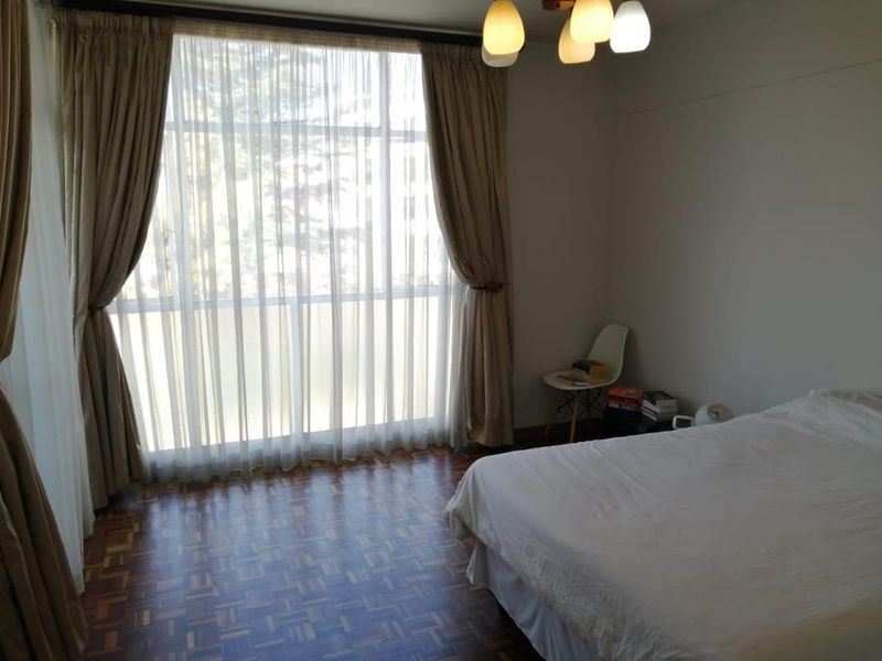A well-lit bedroom featuring classic parquet flooring and a large window with floor-to-ceiling curtains, providing ample natural light.
