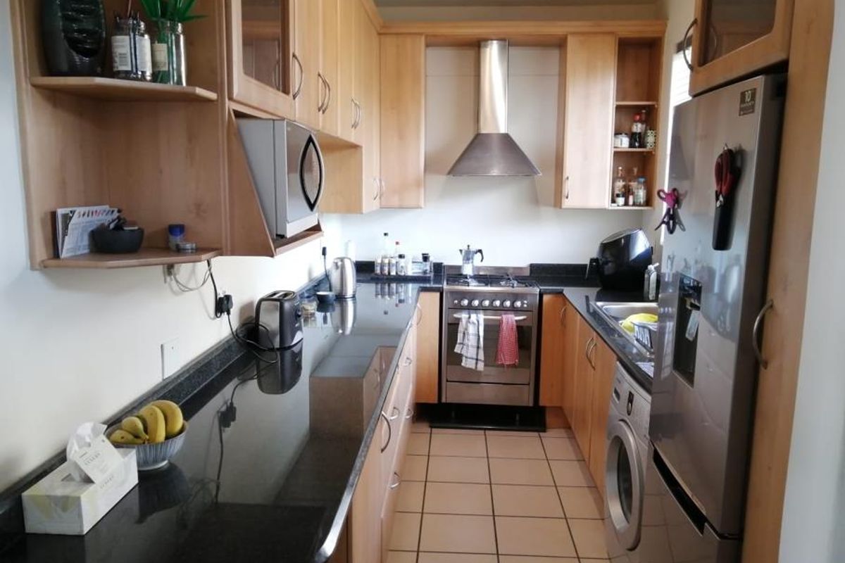 A functional galley-style kitchen featuring light wood cabinetry, dark granite countertops, stainless steel appliances, and tiled flooring.