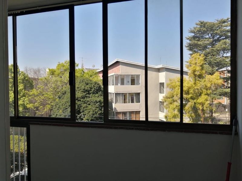 An enclosed balcony area featuring large sliding glass windows with views of the surrounding neighborhood and mature trees.