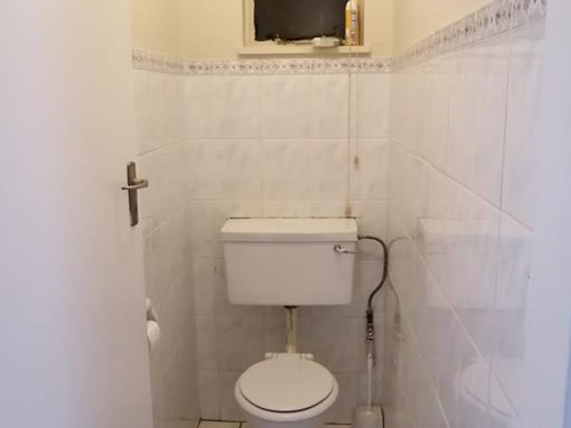 A compact, functional guest toilet featuring white ceramic wall and floor tiles with a small window for ventilation.