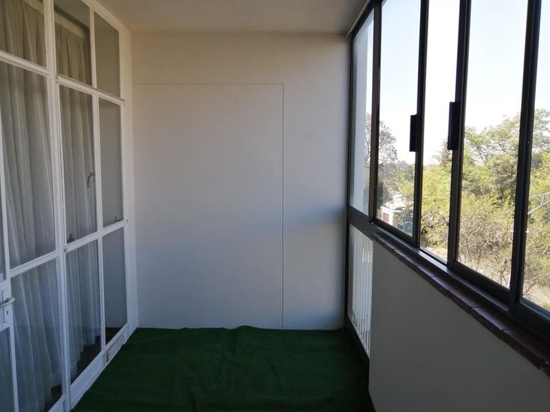 An enclosed balcony featuring aluminum-framed windows and sliding glass doors, offering a bright, versatile space with views of the surrounding greenery.