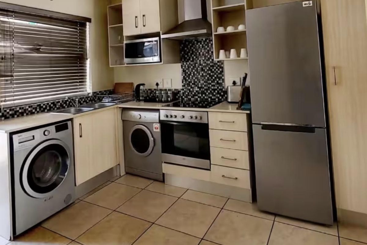 A functional kitchen featuring built-in cabinetry, a mosaic tile backsplash, stainless steel appliances, and tiled flooring.