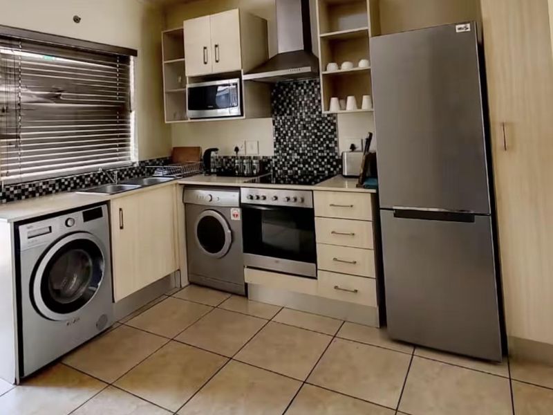 A functional kitchen featuring built-in cabinetry, a mosaic tile backsplash, stainless steel appliances, and tiled flooring.