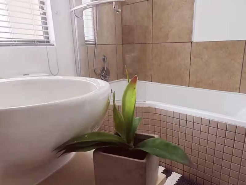 A bathroom featuring a bathtub with a shower mixer, glass screen, and tiled wall finishes, complemented by venetian blinds for privacy.