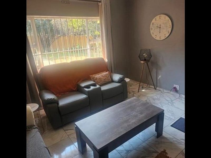 A living room featuring tiled flooring and a large window fitted with security bars, providing natural light to the space.