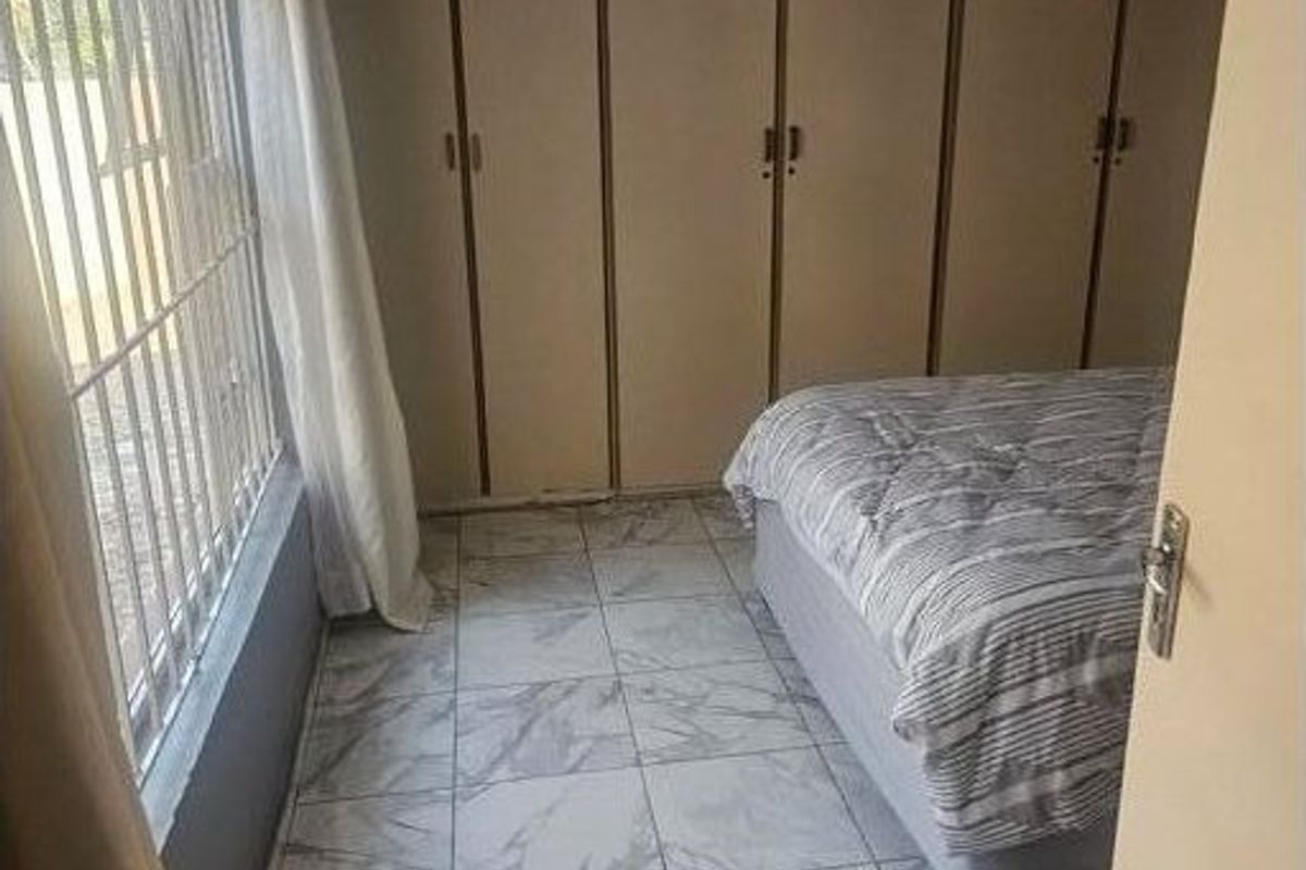 A bedroom featuring built-in cupboards, marble-look tiled flooring, and security bars on the window.