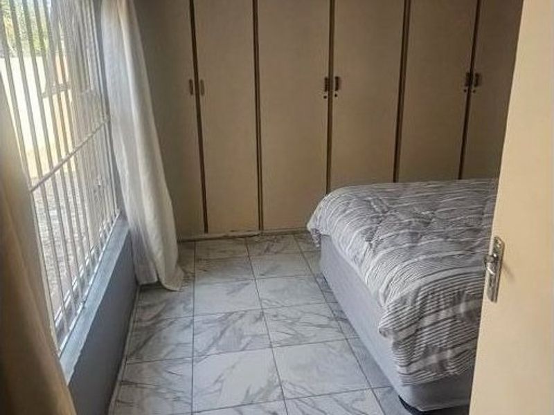 A bedroom featuring built-in cupboards, marble-look tiled flooring, and security bars on the window.