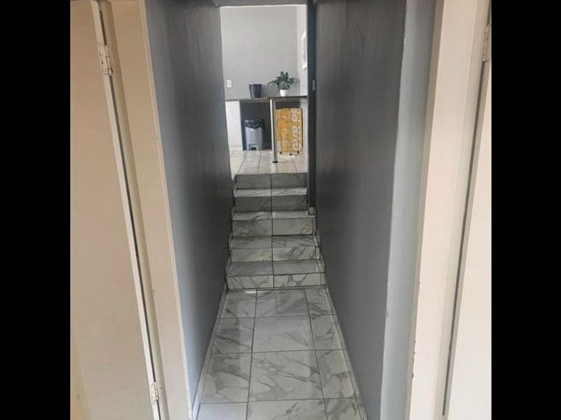 A narrow hallway featuring tiled flooring and a small staircase leading to an adjacent room.