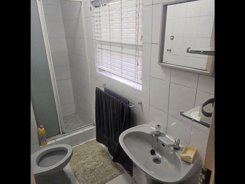 A functional bathroom featuring a shower enclosure, pedestal basin, toilet, and tiled finishes throughout, offering a practical layout for daily use.