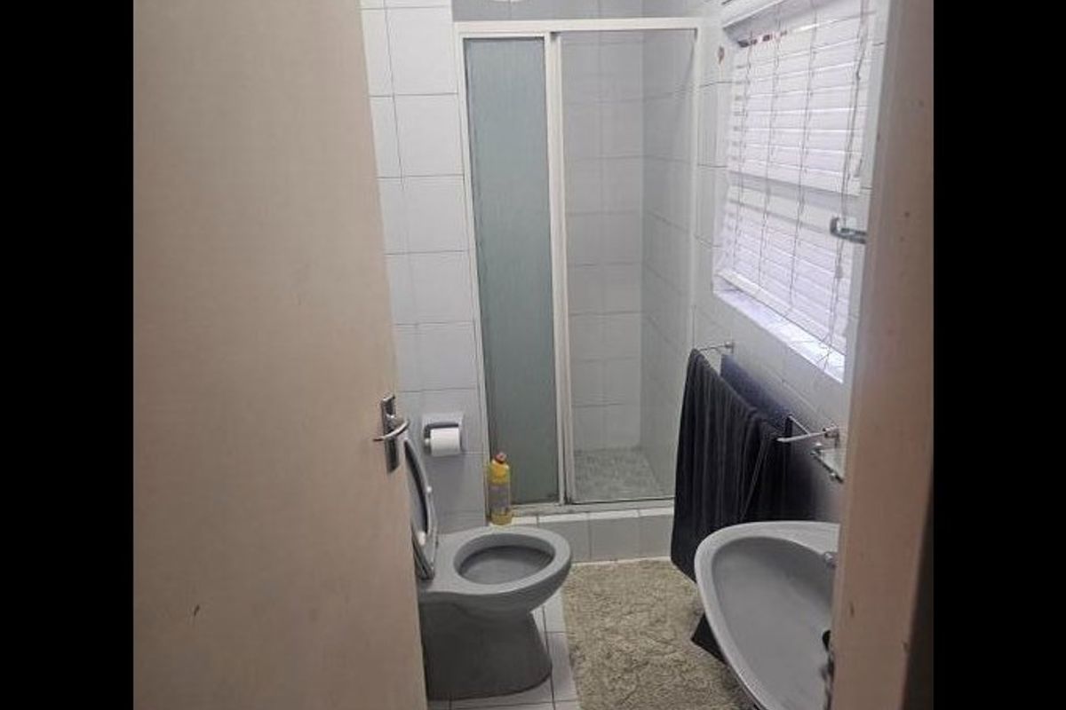 A compact bathroom featuring a shower enclosure, pedestal basin, and toilet with white wall tiling and a window.