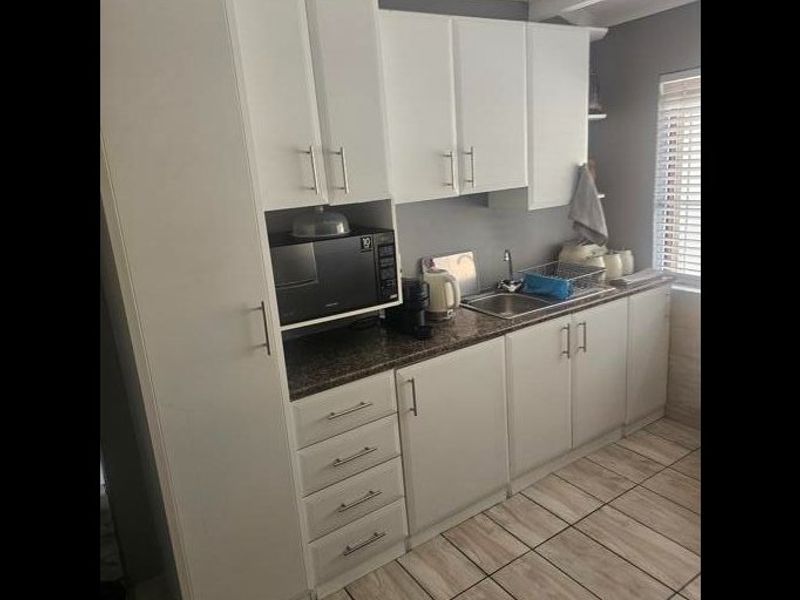 A functional scullery area featuring white built-in cabinetry, a stainless steel sink, laminate countertops, and tiled flooring.