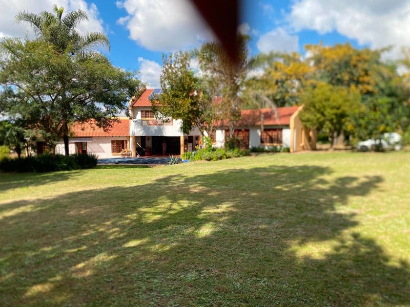 A view of the rear elevation of the house featuring a large garden, mature trees, and a tiled roof with solar panels.