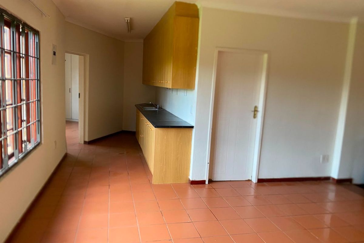 A functional, empty kitchen area featuring laminate cabinetry, a stainless steel sink, and terracotta-style ceramic floor tiles.