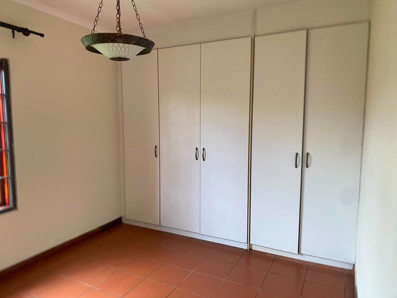 A bright, empty bedroom featuring tiled flooring, built-in cupboards, and a classic pendant light fixture.
