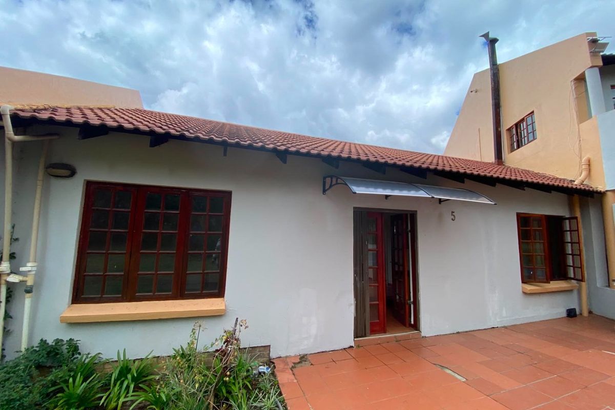 Rear exterior view of the property featuring terracotta roof tiles, paved patio area, and timber-framed windows and doors.