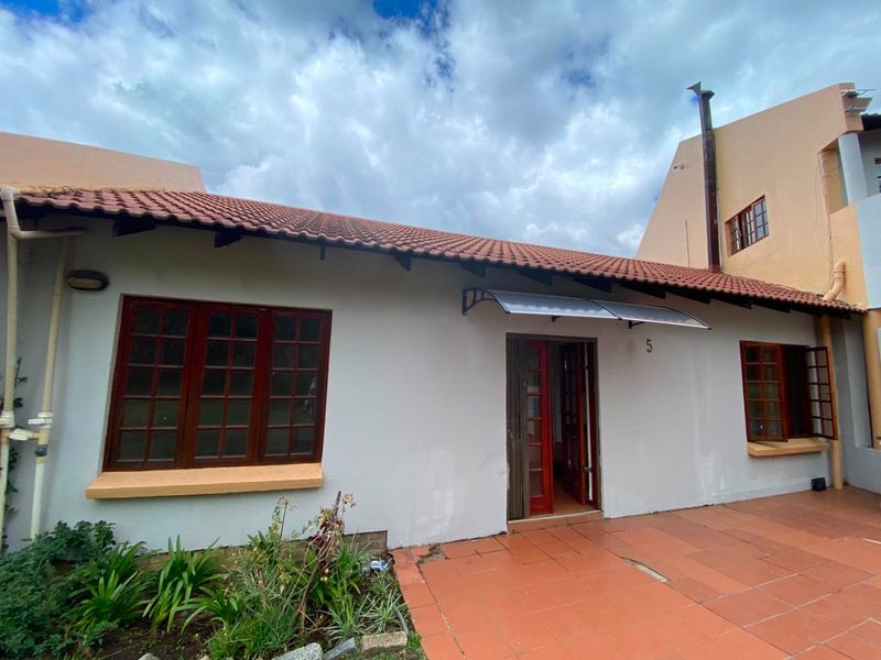 Rear exterior view of the property featuring terracotta roof tiles, paved patio area, and timber-framed windows and doors.