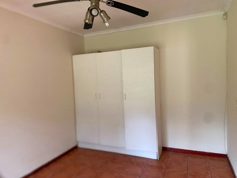 A simple bedroom featuring tiled flooring, a ceiling fan, and a built-in white wardrobe.