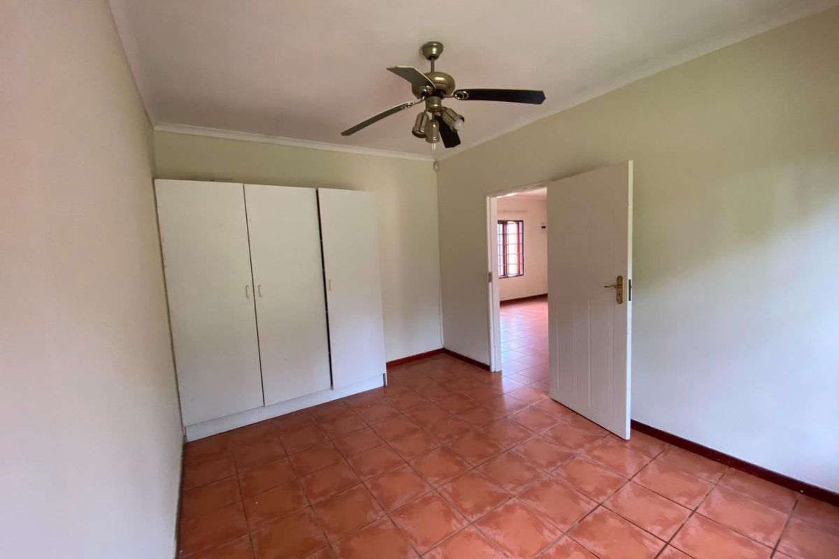 A bright, empty bedroom featuring tiled flooring, a built-in wardrobe, and a ceiling fan, offering a clean canvas for personalization.