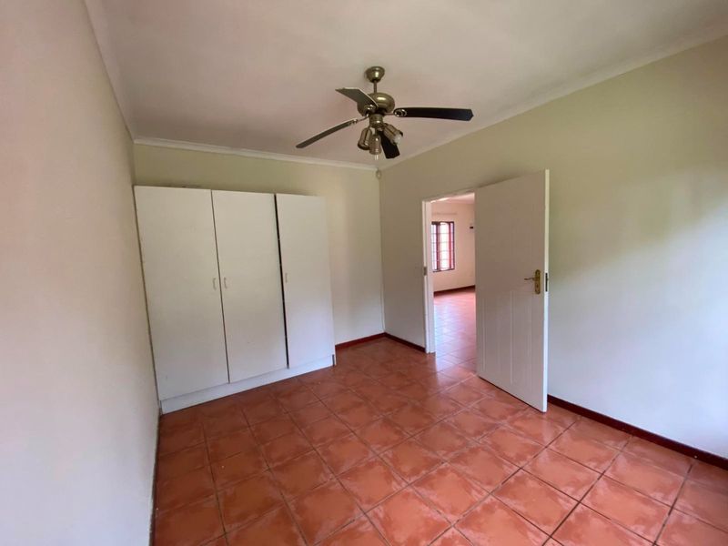 A bright, empty bedroom featuring tiled flooring, a built-in wardrobe, and a ceiling fan, offering a clean canvas for personalization.
