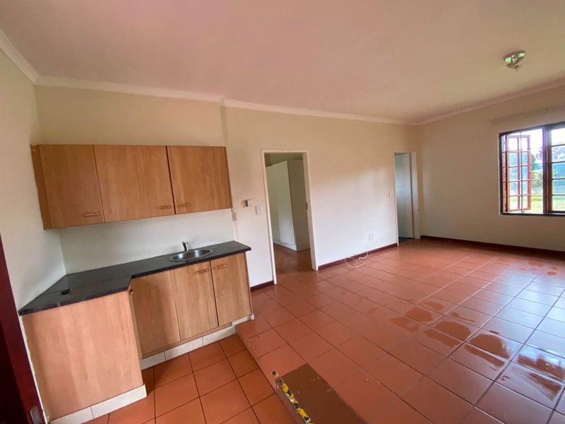 An open-plan living area featuring terracotta floor tiles, a compact kitchenette with wooden cabinetry, and a large window providing natural light.