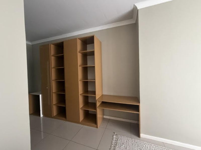 A bedroom featuring neutral walls, tiled flooring, and built-in wooden cabinetry with integrated shelving and desk space.