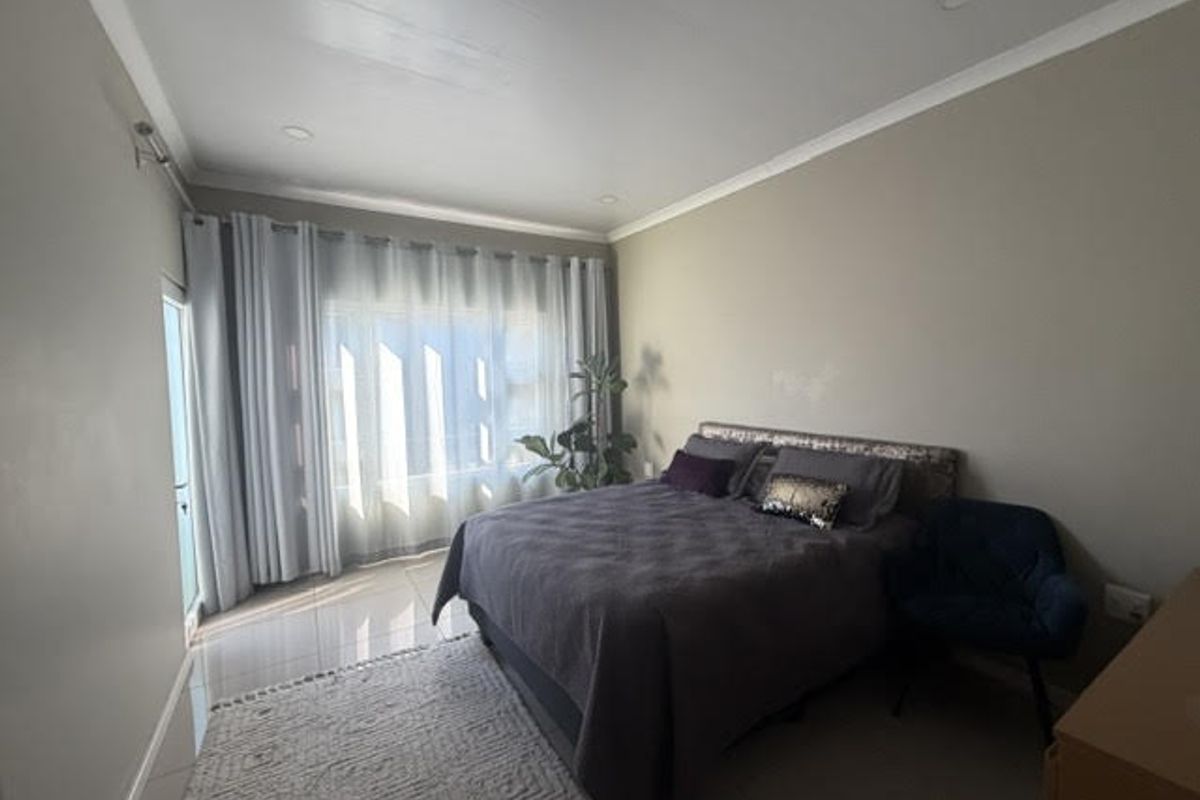 A well-lit bedroom featuring neutral walls, tiled flooring, and a sliding door leading to an outdoor area.