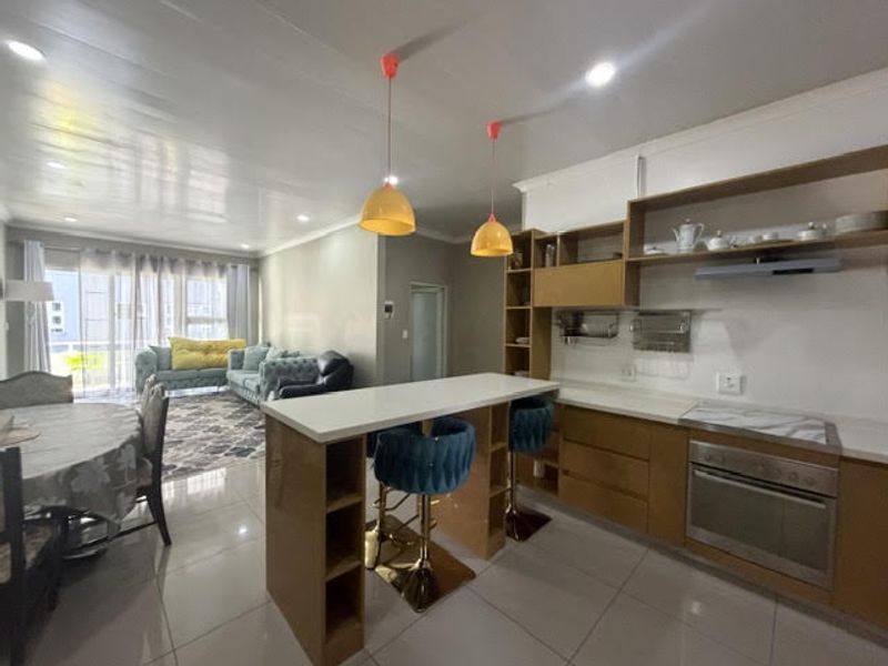 Open plan living and kitchen area featuring a breakfast bar, built-in cabinetry, modern oven, and tiled flooring with access to a balcony.