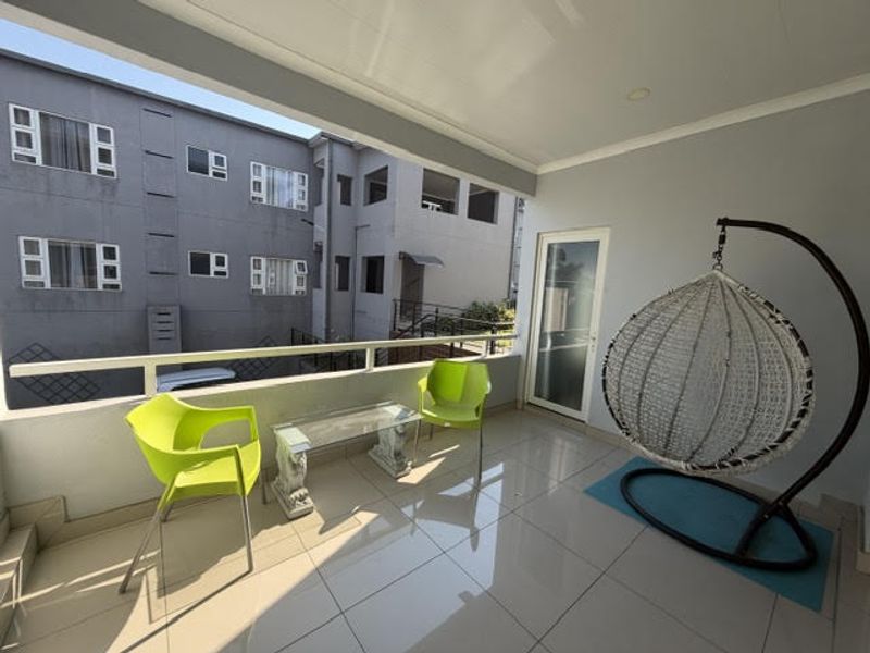 A spacious covered balcony featuring tiled flooring, a secure metal balustrade, and recessed ceiling lighting, offering a pleasant outdoor living area.