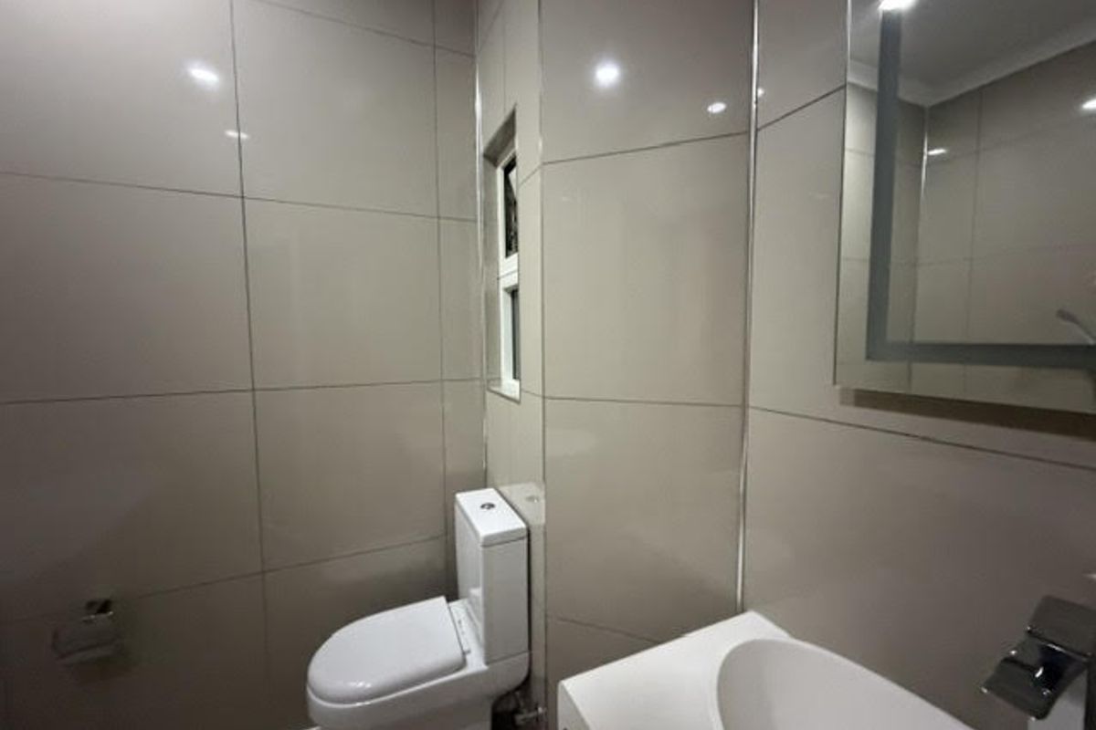 A modern, tiled bathroom featuring a sleek vanity basin, chrome fixtures, an illuminated mirror, and a clean, minimalist design.