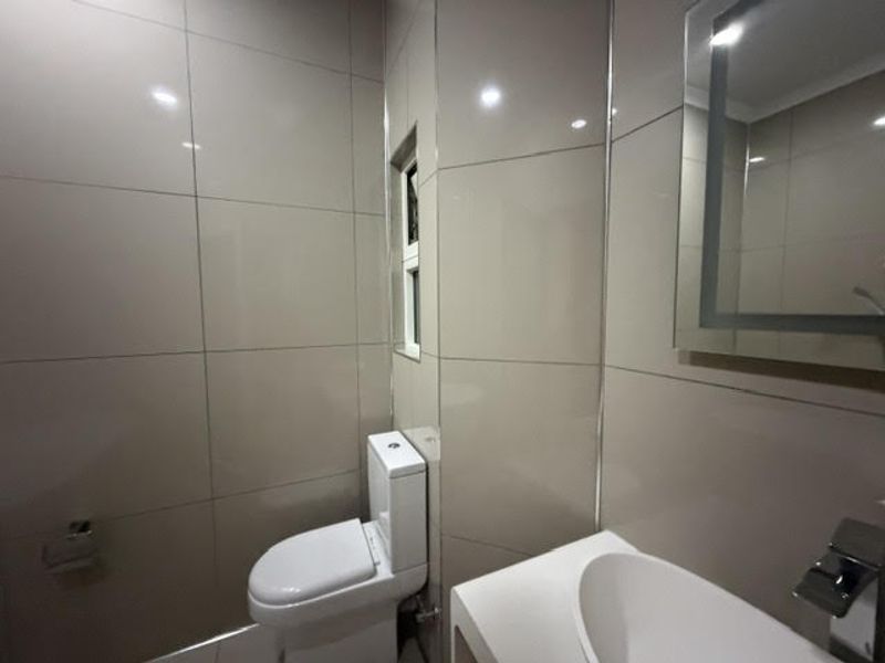 A modern, tiled bathroom featuring a sleek vanity basin, chrome fixtures, an illuminated mirror, and a clean, minimalist design.