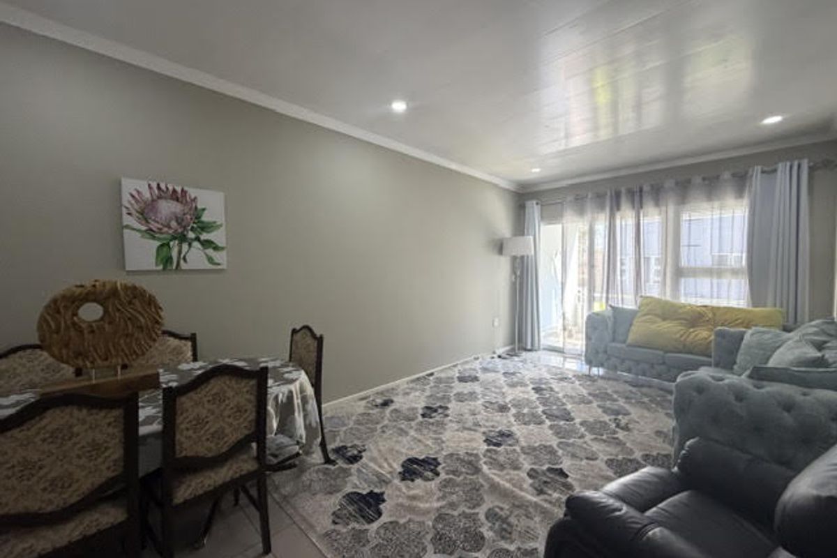 Spacious open-plan living and dining area featuring neutral wall tones, recessed downlighting, tiled flooring, and large sliding glass doors providing natural light.