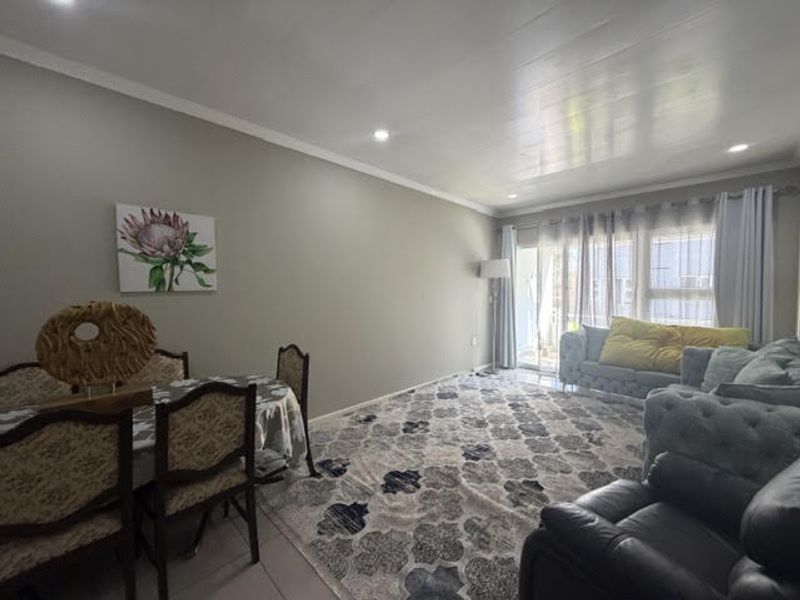Spacious open-plan living and dining area featuring neutral wall tones, recessed downlighting, tiled flooring, and large sliding glass doors providing natural light.