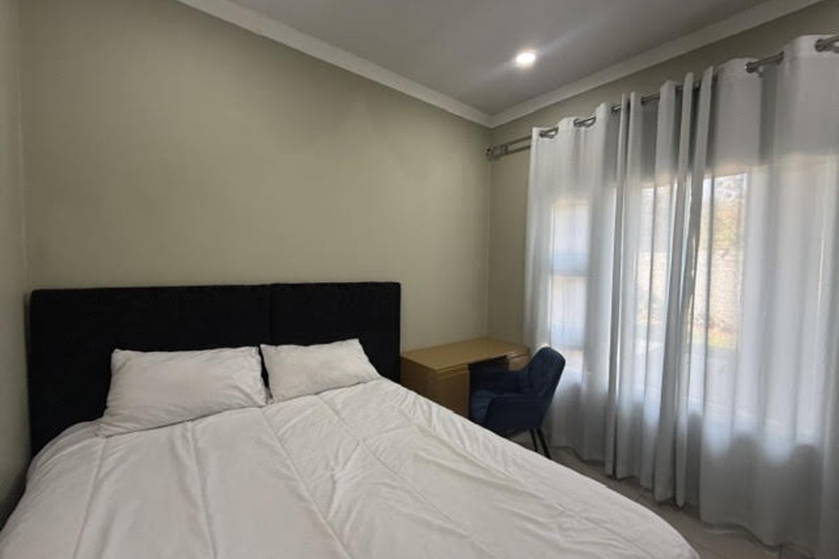 A well-maintained bedroom featuring neutral wall tones, tiled flooring, and large windows dressed with curtains, providing a comfortable and functional living space.