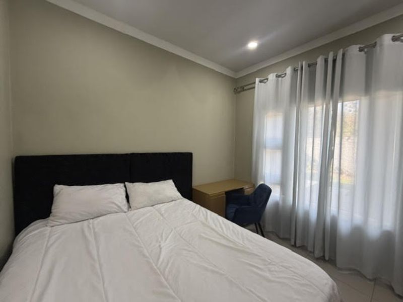 A well-maintained bedroom featuring neutral wall tones, tiled flooring, and large windows dressed with curtains, providing a comfortable and functional living space.