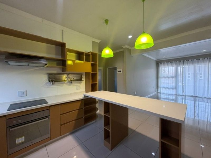 Modern open-plan kitchen featuring built-in oven, electric hob, stone countertops, and a breakfast bar, seamlessly flowing into the living area.