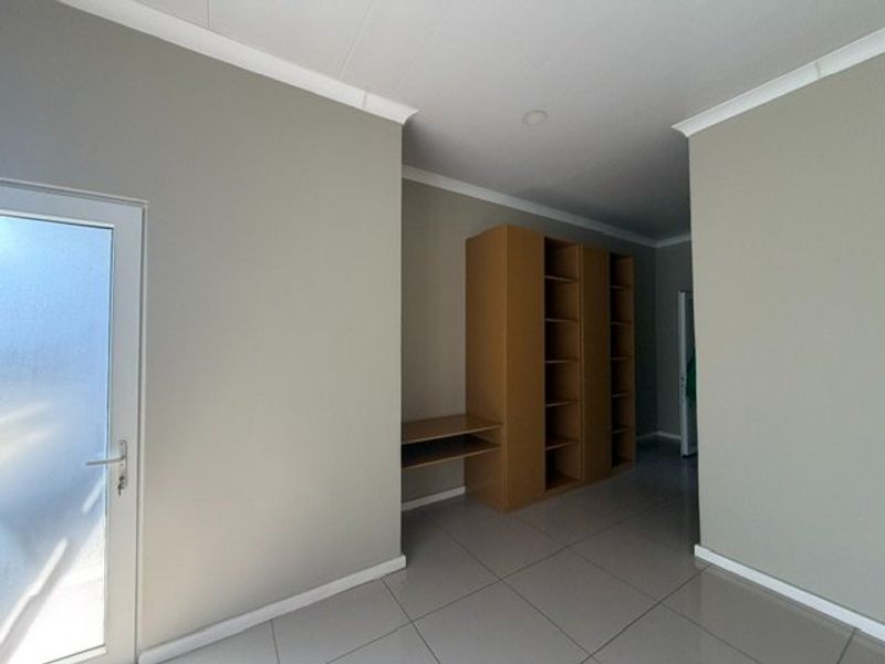 A clean, neutral hallway featuring tiled flooring, built-in shelving units, and a frosted glass door leading to an exterior space.