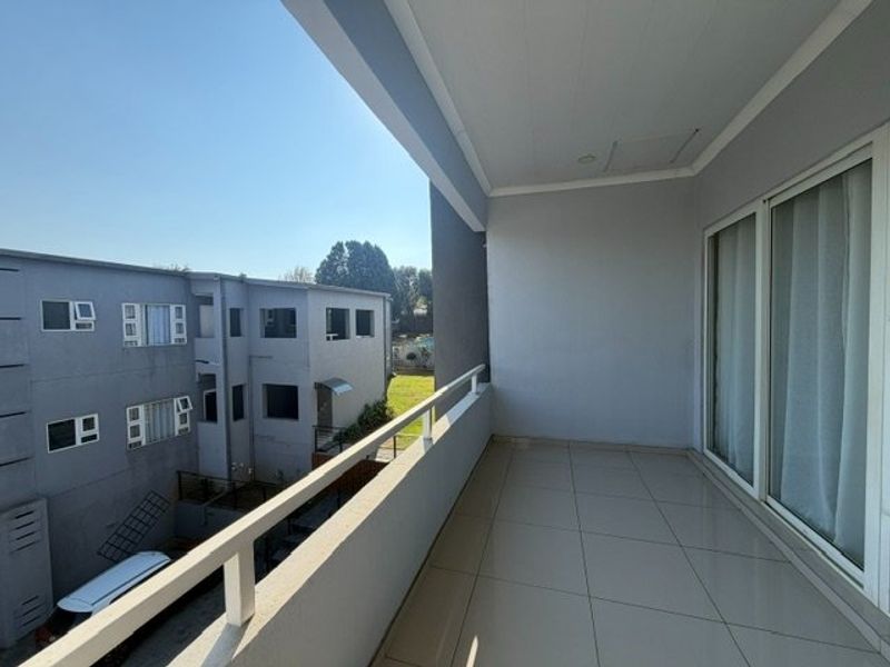 A spacious, covered balcony featuring tiled flooring, a metal balustrade, and large sliding glass doors providing access to the interior.