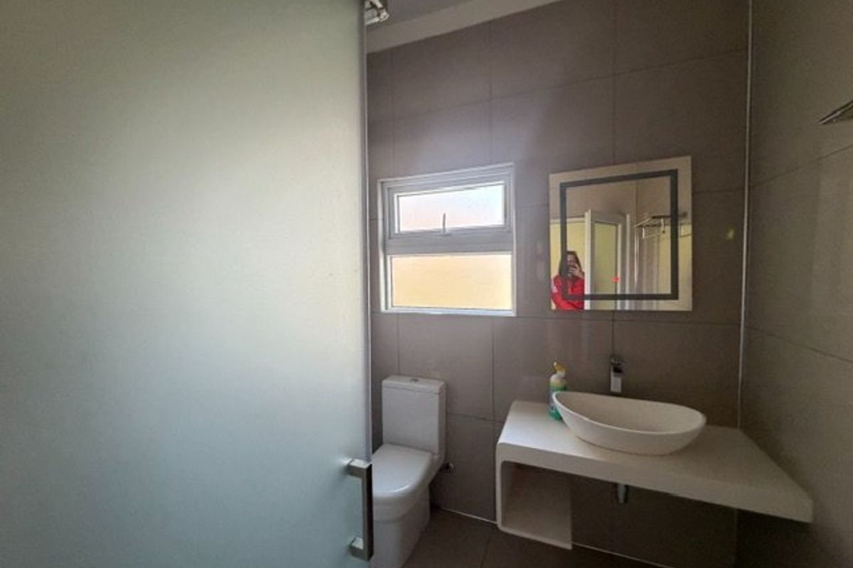 Modern bathroom featuring a vessel sink on a floating vanity, a toilet, and a frosted glass shower enclosure with neutral wall tiling.