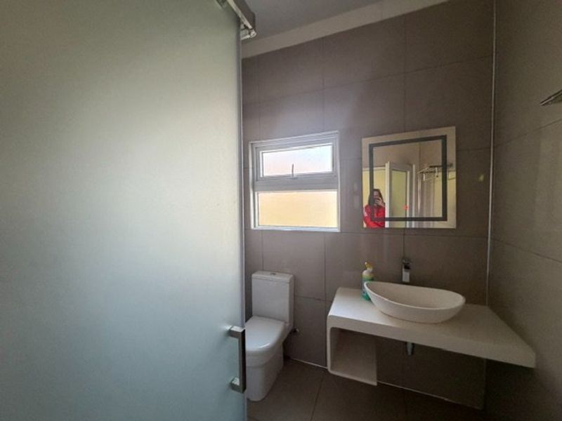 Modern bathroom featuring a vessel sink on a floating vanity, a toilet, and a frosted glass shower enclosure with neutral wall tiling.