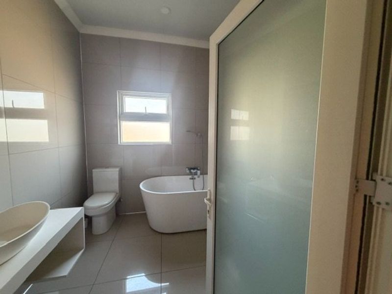 Modern bathroom featuring a freestanding bathtub, vessel sink on a floating vanity, and neutral tiled finishes with a frosted glass entry door.