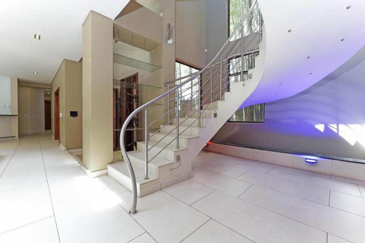 Spacious entrance hall featuring a striking curved staircase with stainless steel balustrade, modern tiled flooring, and integrated accent lighting.