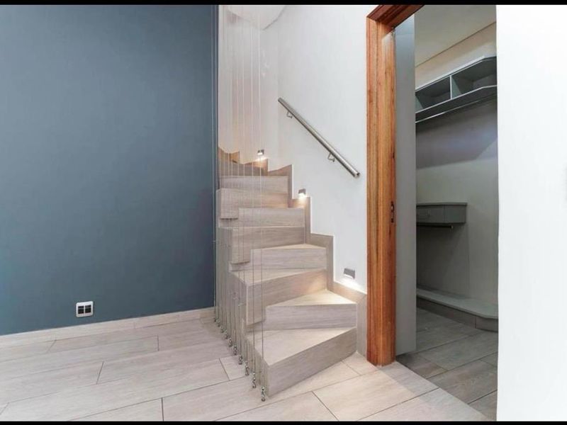 Modern hallway featuring a contemporary staircase with cable balustrade, recessed lighting, and an adjacent walk-in closet with built-in shelving.